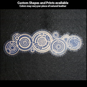 Könnte beinhalten: Ein handbedruckter Leder-Patch mit einem Design aus mehreren konzentrischen Kreisen in Blau und Beige. Der Patch befindet sich auf einem schwarzen Hintergrund. Der Text "Hand Printed Leather Patches" befindet sich oben im Bild. Der Text "Custom Shapes and Prints available" befindet sich unter der ersten Textzeile. Der Text "Colors may vary per piece of natural leather" befindet sich unter der zweiten Textzeile. Der Text "TheGoldenGear.com/HandmadeByDroids.com" befindet sich unten im Bild.