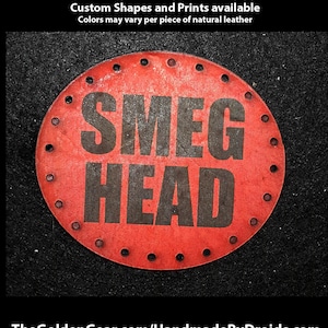 May include: A red leather patch with black lettering that reads "SMEG HEAD". The patch is round and has a circle of small holes around the edge.