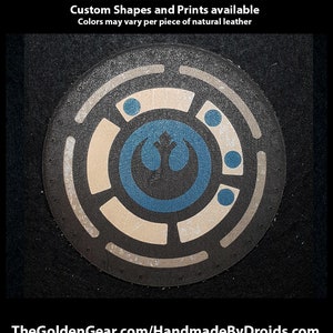 Puede incluir: Un parche de cuero redondo con un símbolo de la Alianza Rebelde en negro, blanco y azul en el centro. El símbolo está rodeado de círculos concéntricos en negro y blanco. El parche está impreso a mano y tiene un aspecto desgastado.