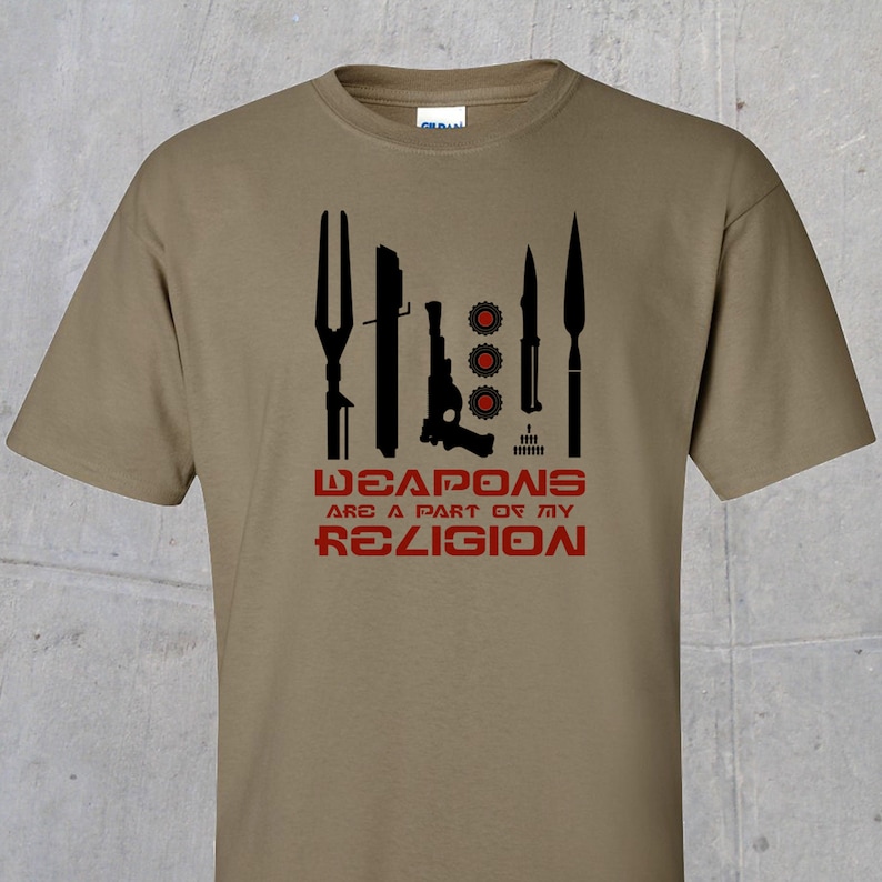 May include: A khaki t-shirt with a black graphic of various weapons and the text "WEAPONS ARE A PART OF MY RELIGION" in red.