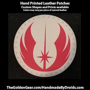 May include: A round, white leather patch with a red and white symbol. The symbol is a stylised representation of a lightsaber with wings. The patch is surrounded by a circle of small holes.