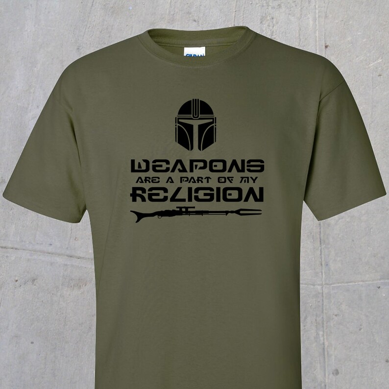 May include: A green t-shirt featuring a black graphic of a Mandalorian helmet and the text "Weapons are a part of my religion".