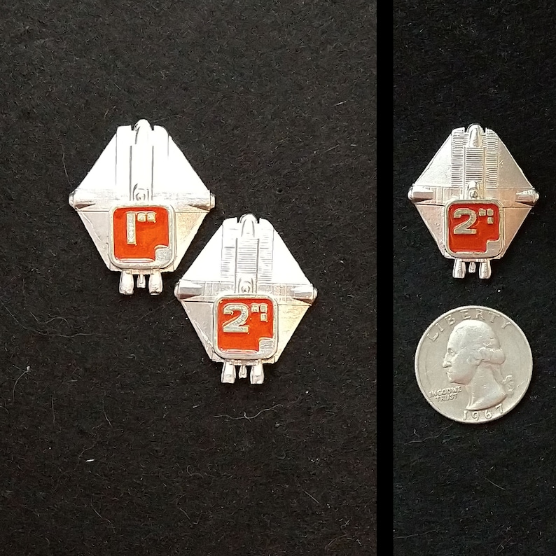 May include: Two silver metal badges with red numbers and the text "2" and "1" on them. The badges are shaped like a diamond with rounded corners and have a design that resembles a spaceship.