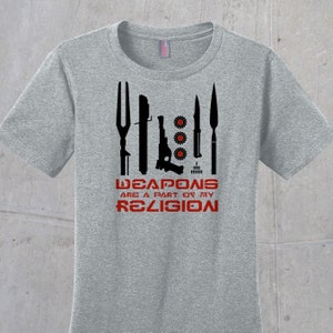 May include: A gray t-shirt with a black graphic of various weapons and the text "WEAPONS ARE A PART OF MY RELIGION".