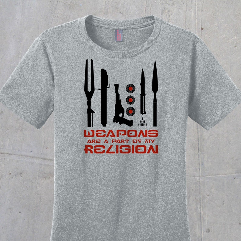 May include: A gray t-shirt with a black graphic of various weapons and the text "WEAPONS ARE A PART OF MY RELIGION".