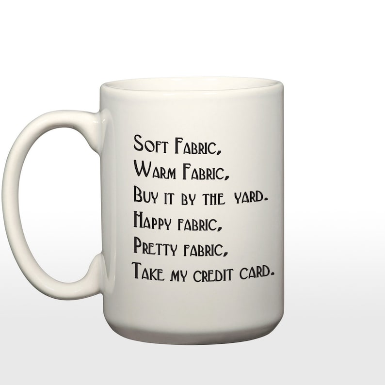 May include: White ceramic coffee mug with black text that reads "SOFT FABRIC, WARM FABRIC, BUY IT BY THE YARD. HAPPY FABRIC, PRETTY FABRIC, TAKE MY CREDIT CARD."