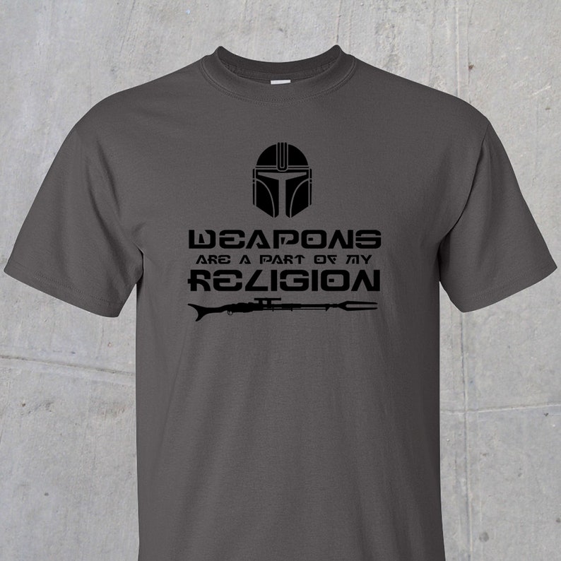 May include: A dark grey t-shirt with a black graphic of a Mandalorian helmet and the text "Weapons are a part of my religion".