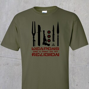 May include: A green t-shirt with a black graphic of various weapons and the text "WEAPONS ARE A PART OF MY RELIGION" in red.