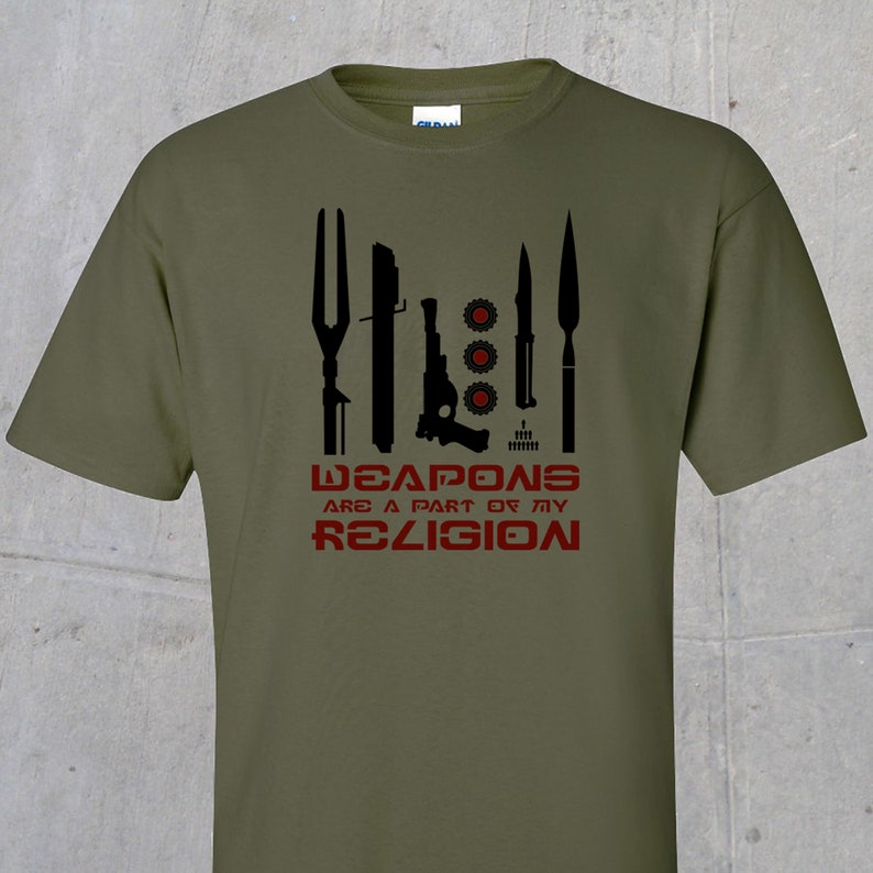 May include: A green t-shirt with a black graphic of various weapons and the text "WEAPONS ARE A PART OF MY RELIGION" in red.