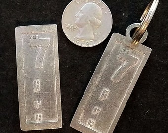 May include: Two silver metal key tags with the number "7" engraved on them. The key tag on the right has a key ring attached to it.