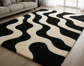 May include: A rectangular area rug with a bold, wavy pattern in black and cream. The rug is placed on a hardwood floor in a living room setting, with a gray sofa and a potted plant visible in the background. The design creates a striking visual contrast.