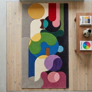 May include: A colorful, abstract area rug with a geometric design. The rug features a variety of shapes and colors, including yellow, red, green, blue, and purple. The rug is rectangular and appears to be made of a soft material.