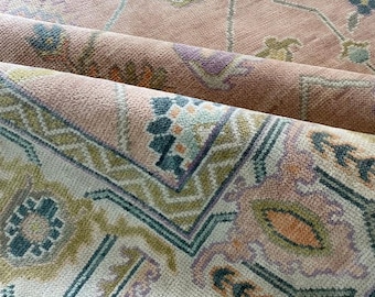 May include: Close-up of a rolled-up area rug with a floral pattern. The rug features a soft pink background with intricate designs in shades of green, purple, and orange. The edges of the rug are visible, showcasing the texture and detail of the weave.