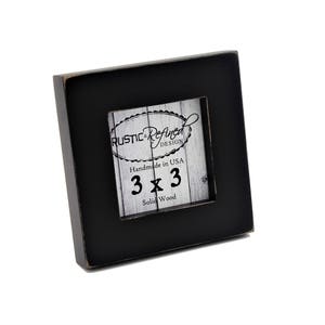 May include: A square black picture frame with a smaller square opening. The frame has a distressed finish. The center features a printed design with the text "Rustic & Refined Design" and "3 x 3 Solid Wood". Handmade in USA.