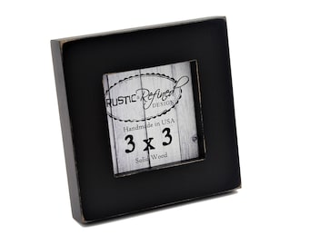 Puede incluir: Un marco de fotos cuadrado de madera negra con bordes desgastados. El inserto presenta el texto "RUSTIC & REFINED DESIGN", "Handmade in USA", "3 x 3" y "Solid Wood" impreso sobre un fondo con patrón de veta de madera blanca.