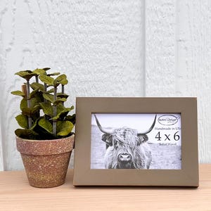 Pode incluir: Uma moldura de madeira dourada com uma fotografia preto e branco de uma vaca das terras altas dentro. A moldura mede 10,16 x 15,24 cm e diz "Handmade in USA, Solid Wood" na parte inferior.