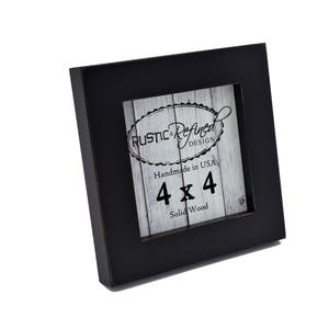 May include: A square black wooden picture frame with a 4 x 4 inch opening. The frame has a white and gray insert with the text "RUSTIC & Refined DESIGN" and "Handmade in USA".