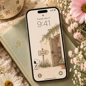 May include: A smartphone displays a charming illustration of Snoopy in front of a bookstore. The screen shows the time as 9:41 AM on Tuesday, May 14th. The phone rests on a vintage green book, surrounded by flowers and a floral-decorated mug.