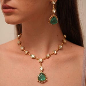 Può includere: Un set composto da collana e orecchini pendenti color oro con pietre triangolari verdi. La collana presenta una catenina con piccole pietre rotonde e trasparenti distanziate uniformemente, terminante con un pendente centrale verde.