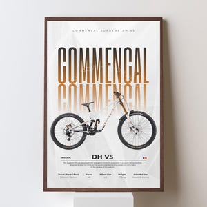 May include: A framed poster featuring a white Commencal DH V5 mountain bike. The bike has black tires, a gold fork, and is set against a gradient background. The poster includes the text "COMMENCAL" and "DH V5".