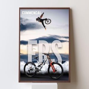 May include: Framed poster featuring a mountain bike and a cyclist mid-air. The poster has the word "COMMENCAL" at the top and the word "FRS" in large letters. The bike has orange and black accents. The background is a cloudy sky.