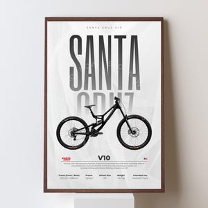 Può includere: Un poster incorniciato con una mountain bike Santa Cruz V10 nera. Il poster mostra il testo "SANTA CRUZ V10" a grandi lettere in grassetto. Le specifiche, tra cui le dimensioni delle ruote e il peso, sono elencate sotto la bici. Lo sfondo è bianco con sottili linee grigie.