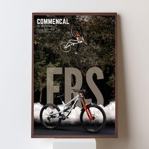 Könnte beinhalten: Gerahmtes Poster mit einem Mountainbike in der Luft, mit dem Wort "COMMENCAL" oben. Das Fahrrad hat orangefarbene und weiße Akzente. Die Buchstaben "FRS" sind deutlich sichtbar. Der Hintergrund zeigt einen Wald und einen Fahrer.