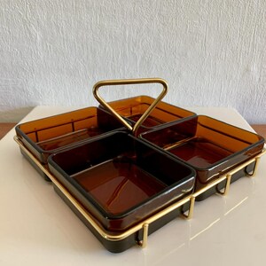Peut inclure: Un plateau de service vintage de couleur ambre avec quatre compartiments carrés. Le plateau a une poignée dorée et un cadre en métal doré. Le plateau est conçu pour servir des collations ou des apéritifs.