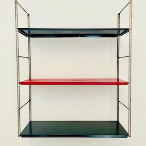 May include: A wall-mounted shelving unit featuring three horizontal shelves supported by two vertical metal ladder-style frames. The top and bottom shelves are dark green, while the middle shelf is bright red. The side supports are gold-toned.