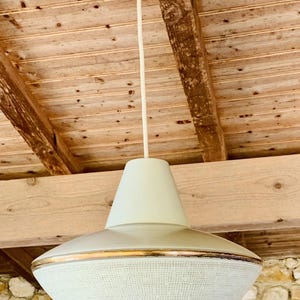 May include: A retro pendant light fitting with a white ceiling rose and a long, thin white cable. The light has a pale green conical top and a wide, rounded shade with a textured, off-white surface and gold trim.