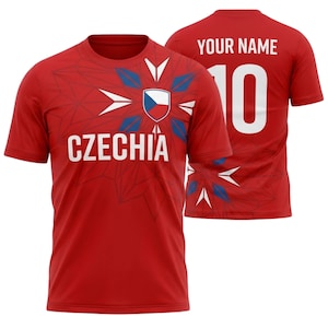 Op de afbeelding: Rood t-shirt met "CZECHIA" in witte letters en een embleem van Tsjechië. De achterkant van het shirt toont "YOUR NAME" boven het nummer "10" in wit. Het shirt heeft een geometrisch ontwerp.