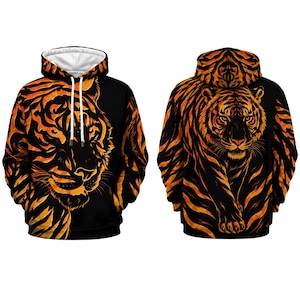 Può includere: Una felpa con cappuccio nera caratterizzata da una grafica di tigre color arancione vivace. Il davanti mostra un primo piano del muso di una tigre, mentre il retro presenta un'illustrazione a figura intera. Include un cappuccio con lacci bianchi.