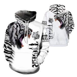 May include: A white hoodie featuring a black tiger stripe pattern and a large graphic of a roaring white tiger with its mouth open. The word TIGER is printed vertically in black lettering on the front and back, accompanied by a small tiger head icon.