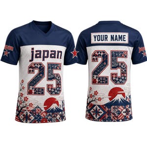 Puede incluir: Una camiseta de cuello en V azul marino y blanca con la palabra japan y el número 25 en el frente. La parte posterior muestra el texto YOUR NAME sobre el número 25. El diseño incluye patrones de sol rojo, montaña y flores en la parte inferior.