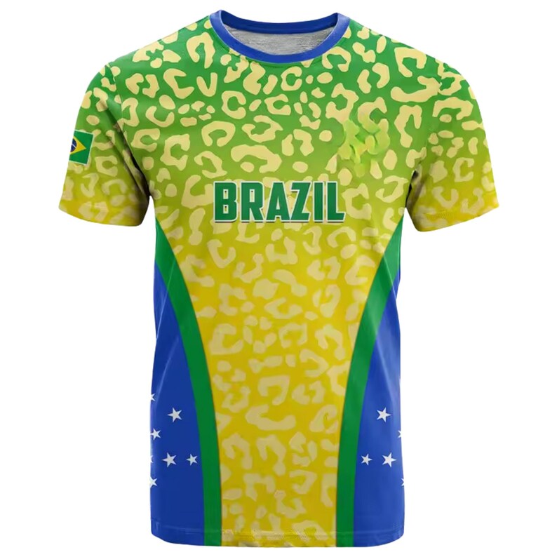 May include: A short-sleeved t-shirt with a vibrant design featuring the word "BRAZIL" in green block letters. The shirt has a yellow and green leopard print pattern on the top, with blue and white accents on the sides. A small Brazilian flag is visible.