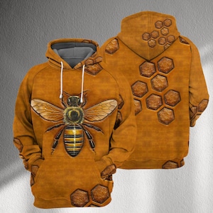 May include: A brown hoodie with a large bee design on the front, showing yellow and black stripes and detailed wings. The back of the hoodie has a honeycomb pattern. The hoodie has a grey hood lining and white drawstrings.