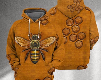 Könnte beinhalten: Ein brauner Kapuzenpullover mit einem großen Bienenmuster auf der Vorderseite. Die Biene hat gelbe und schwarze Streifen und detaillierte Flügel. Die Rückseite des Kapuzenpullovers hat ein Wabenmuster. Der Kapuzenpullover hat ein graues Kapuzenfutter und weiße Kordelzüge.