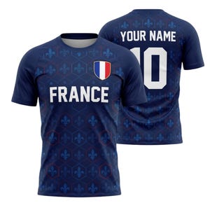 May include: Navy blue short-sleeve jersey with the word "FRANCE" in white on the front. The jersey features a French flag emblem and a pattern of blue fleur-de-lis. The back displays "YOUR NAME" and the number "10" in white.