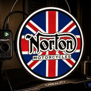 Può includere: Un'insegna rotonda con il design della bandiera Union Jack e la scritta "Norton MOTORCYCLES". L'insegna ha un bordo al neon bianco. Una fotocamera nera e un display digitale con temperature in gradi Celsius sono visibili.