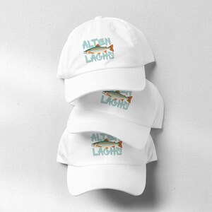 Könnte beinhalten: Stapel von drei weißen Baseballkappen. Jede Kappe zeigt eine Fischgrafik mit dem Text "ALTEN LAGHS" in Blau. Der Fisch ist in Grün, Orange und Braun dargestellt.