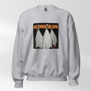 Könnte beinhalten: Ein hellgraues Sweatshirt mit einer Grafik von drei Gänsen in weißen Umhängen. Die Grafik trägt den Text "GOOSEBUMPS" in orangefarbenen Buchstaben. Das Sweatshirt hat einen Rundhalsausschnitt und lange Ärmel.