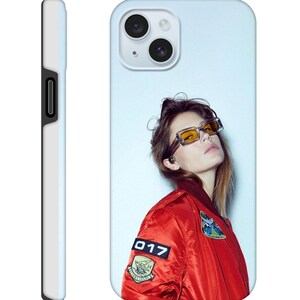 Può includere: Custodia per telefono con un design di giacca bomber rossa, con toppe e il numero "017". La custodia mostra anche una persona con occhiali da sole gialli. La custodia ha uno sfondo azzurro e un lato bianco.
