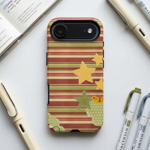 May include: A phone case with a colorful design featuring horizontal stripes in shades of red, green, and brown. The case is adorned with yellow stars and green cloud-like shapes. The case is surrounded by pens and a notebook.