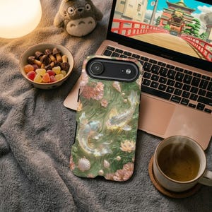 Green floral koi fish phone case on a gray blanket beside an open laptop, a mug of coffee and a small bowl of snacks.