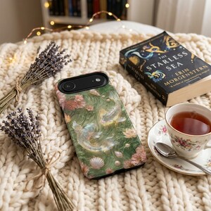 Green floral koi fish phone case on a cream knitted blanket beside a cup of tea, dried flowers and a closed book.