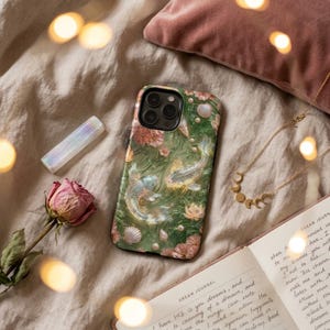 Green koi fish phone case on soft ivory fabric with warm string lights, a dried pink rose, rose quartz and a printed page.