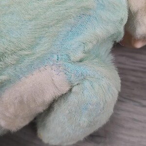 Op de afbeelding: Close-up van de poot en het lichaam van een pluche speelgoed. Het speelgoed is gemaakt van zacht, pluizig materiaal in lichtblauw en wit. Zichtbare stiksels duiden op een reparatie. De vacht van het speelgoed heeft een licht versleten uiterlijk.