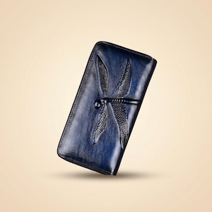 May include: A rectangular navy blue wallet featuring a prominent embossed dragonfly design on the front surface. The wallet has a smooth, polished finish with a dark blue gradient effect and a zip closure along the side edge of the item.