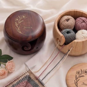 May include: A wooden yarn bowl and a yarn holder with the name "Jessica" engraved. The yarn bowl contains several balls of yarn in neutral colors. Knitting needles are in use with a partially completed knitted piece.