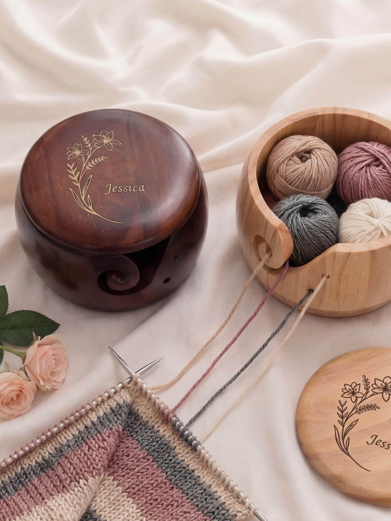 May include: A wooden yarn bowl and a yarn holder with the name "Jessica" engraved. The yarn bowl contains several balls of yarn in neutral colors. Knitting needles are in use with a partially completed knitted piece.